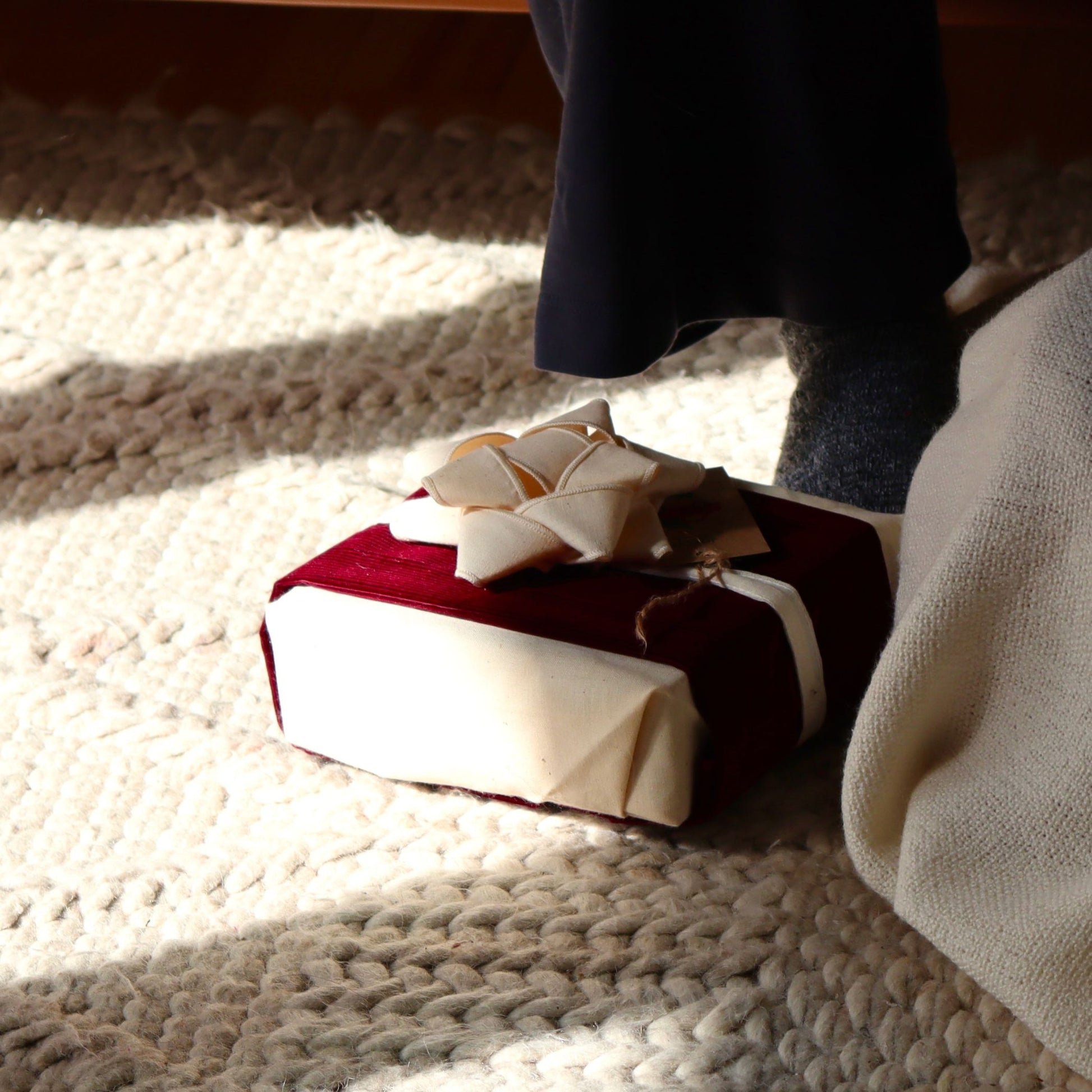 Emballage cadeau en tissu avec un chou a cadeau réutilisable posé au sol, couleur crème et bourgogne